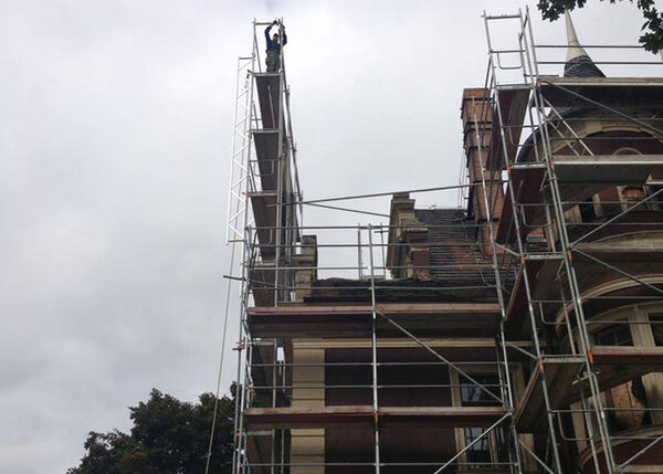 Ein Bauarbeiter steht auf hohem Gerüst an historischer Fassade bei Sanierungsarbeiten.