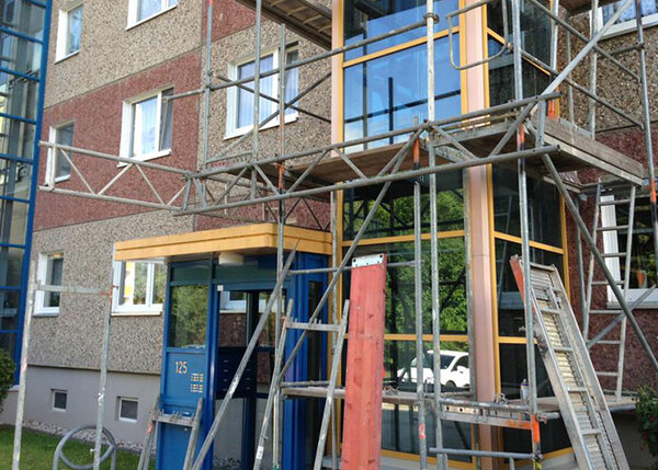 Fassadensanierung an einem Mehrfamilienhaus mit Gerüstbau und modernem Eingangsbereich.