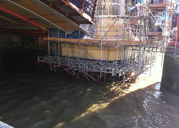 Brückensanierung mit Baugerüst über Wasser, Bauarbeiten an Brückenfundament sichtbar.