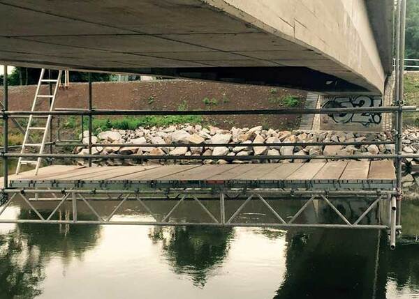 Arbeitsgerüst unter einer Brücke über einem Fluss mit Baugerüst und Leiter zur Brückeninspektion.