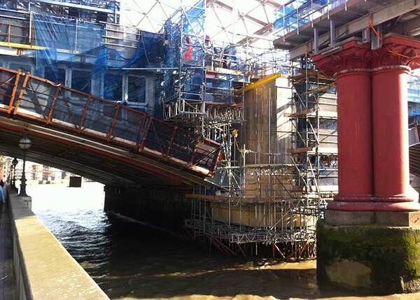Brücke mit Baugerüsten über einem Fluss bei Sanierungsarbeiten und roten Säulen.