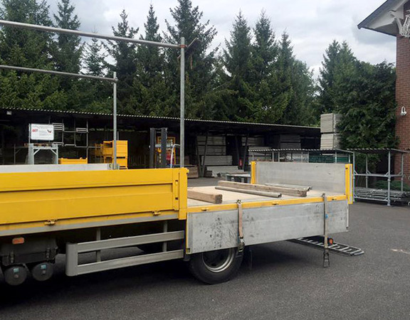 Offener LKW mit gelber Bordwand steht auf Lagerplatz für Baustellenausstattung.