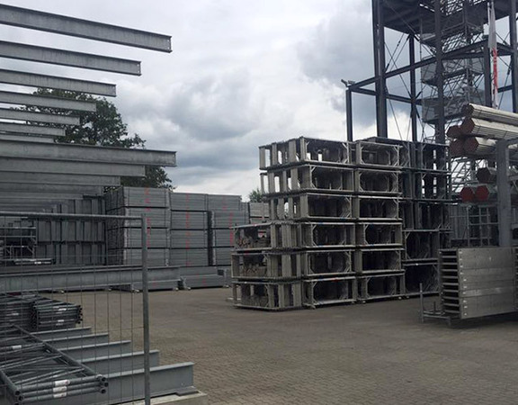 Stapel von Gerüstbau-Material und Metallträgern auf einem Lagerplatz im Freien.